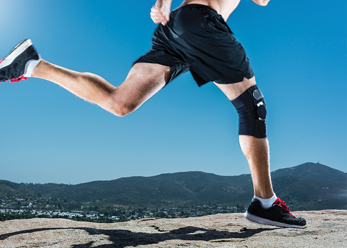 Person with an orthotic brace on their knee running outside.