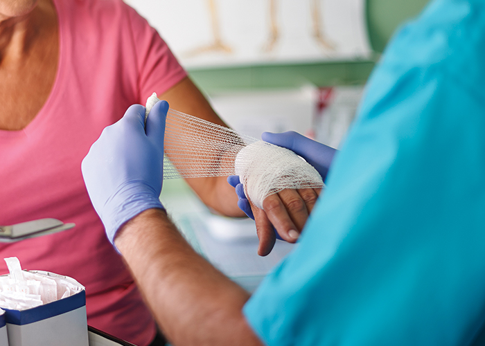 Photo featuring a medical professional applying gauze to a hand wound.